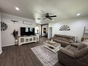 Una sala de estar con televisor, mueble blanco, sofá marrón, alfombra estampada y elementos decorativos en la pared.