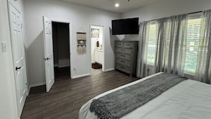 A bedroom with a bed, a ceiling fan, a TV, a dresser, and a window with curtains.