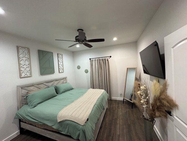 Un dormitorio con cama, ventilador de techo, televisión instalada en la pared y espejos decorativos.