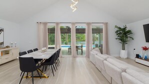 A modern dining area with a long table and chairs, a sofa, and a view of a swimming pool.