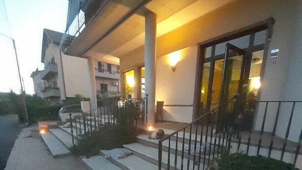 A building with a covered entrance, steps leading up to a door, and a small garden area with a bench. - Panoramik  (Acri)