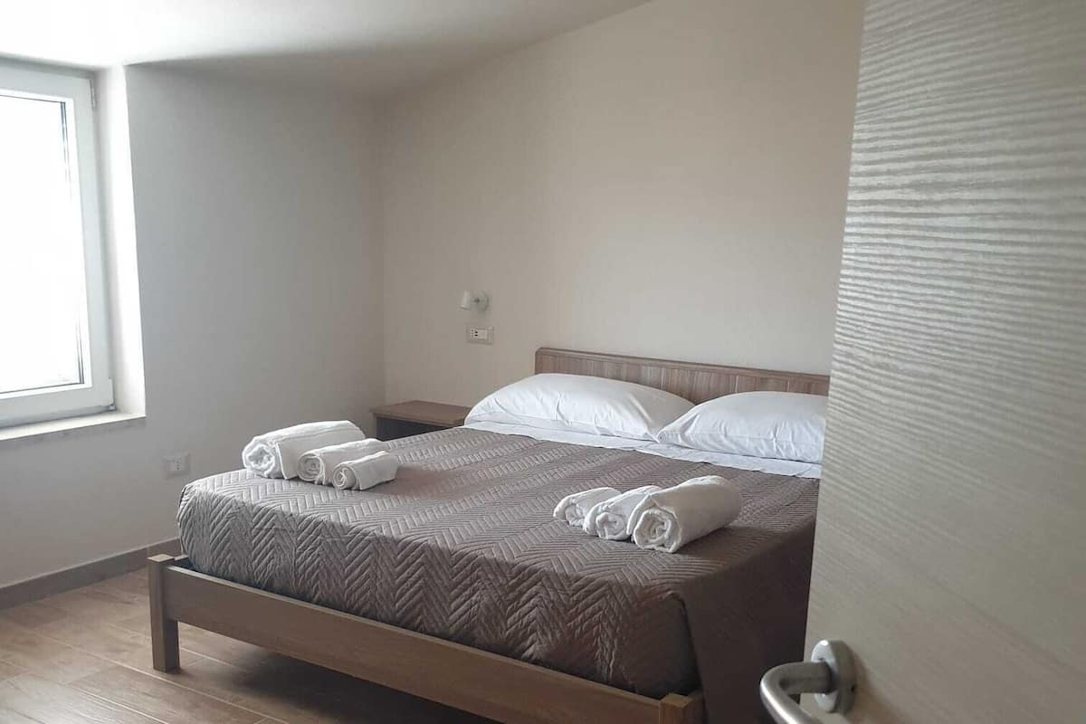A neatly made bed with rolled towels, a wooden headboard, and a wooden floor.