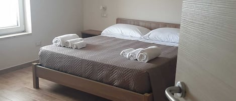 A neatly made bed with rolled towels, a wooden headboard, and a wooden floor.