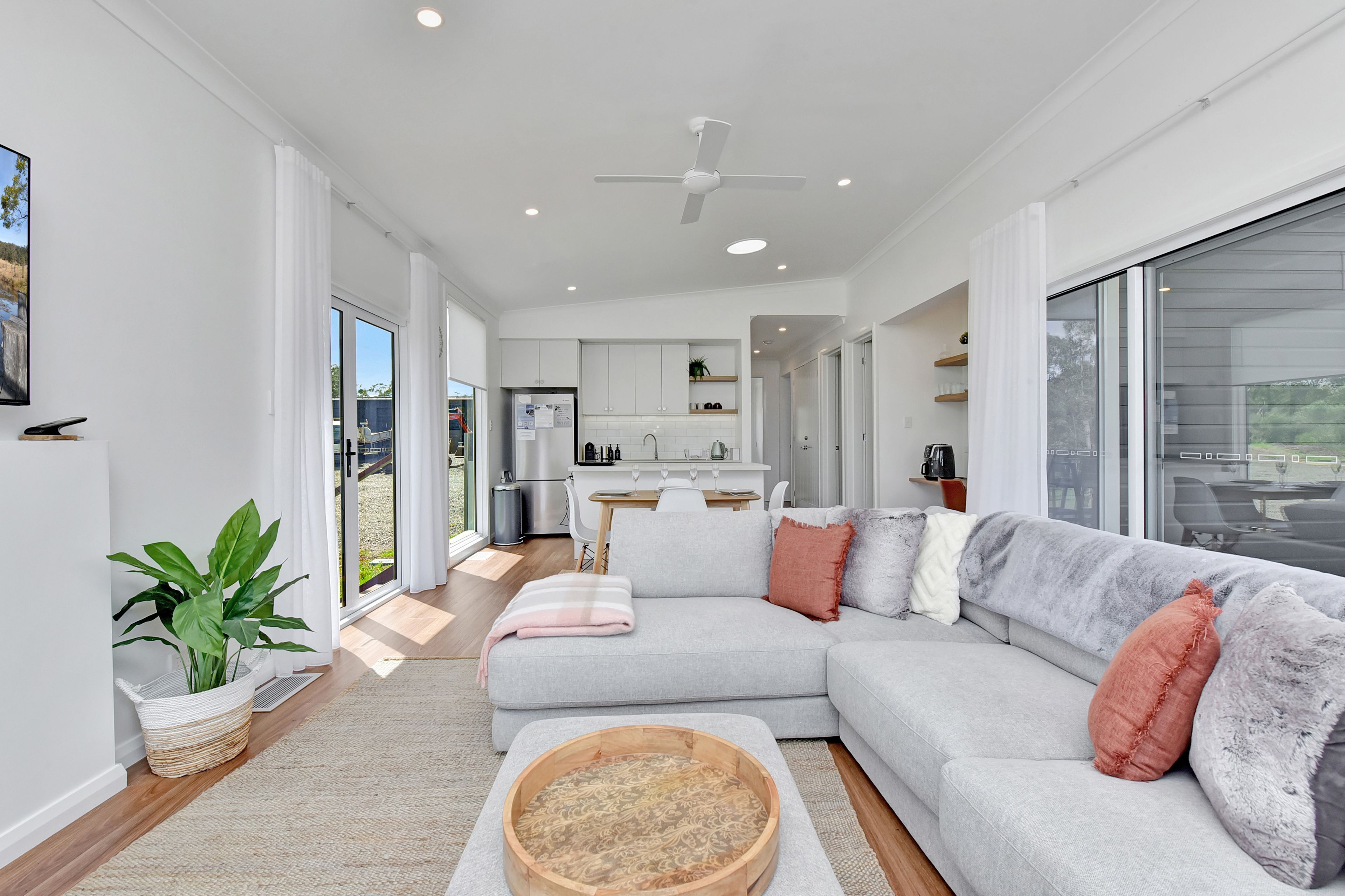 A modern living room with a sectional sofa, a wooden coffee table, and a view of the kitchen and outdoor area.