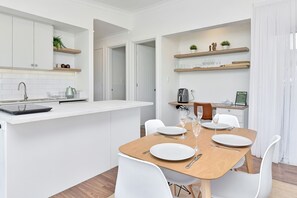 Une cuisine moderne avec des meubles blancs, une table à manger en bois pour quatre personnes et une machine à café.