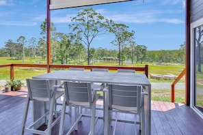 An outdoor deck with a table and chairs, overlooking a grassy area with trees and a body of water.