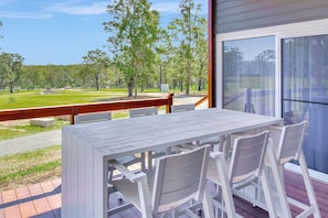 An outdoor patio with a table and chairs, overlooking a grassy area with trees.