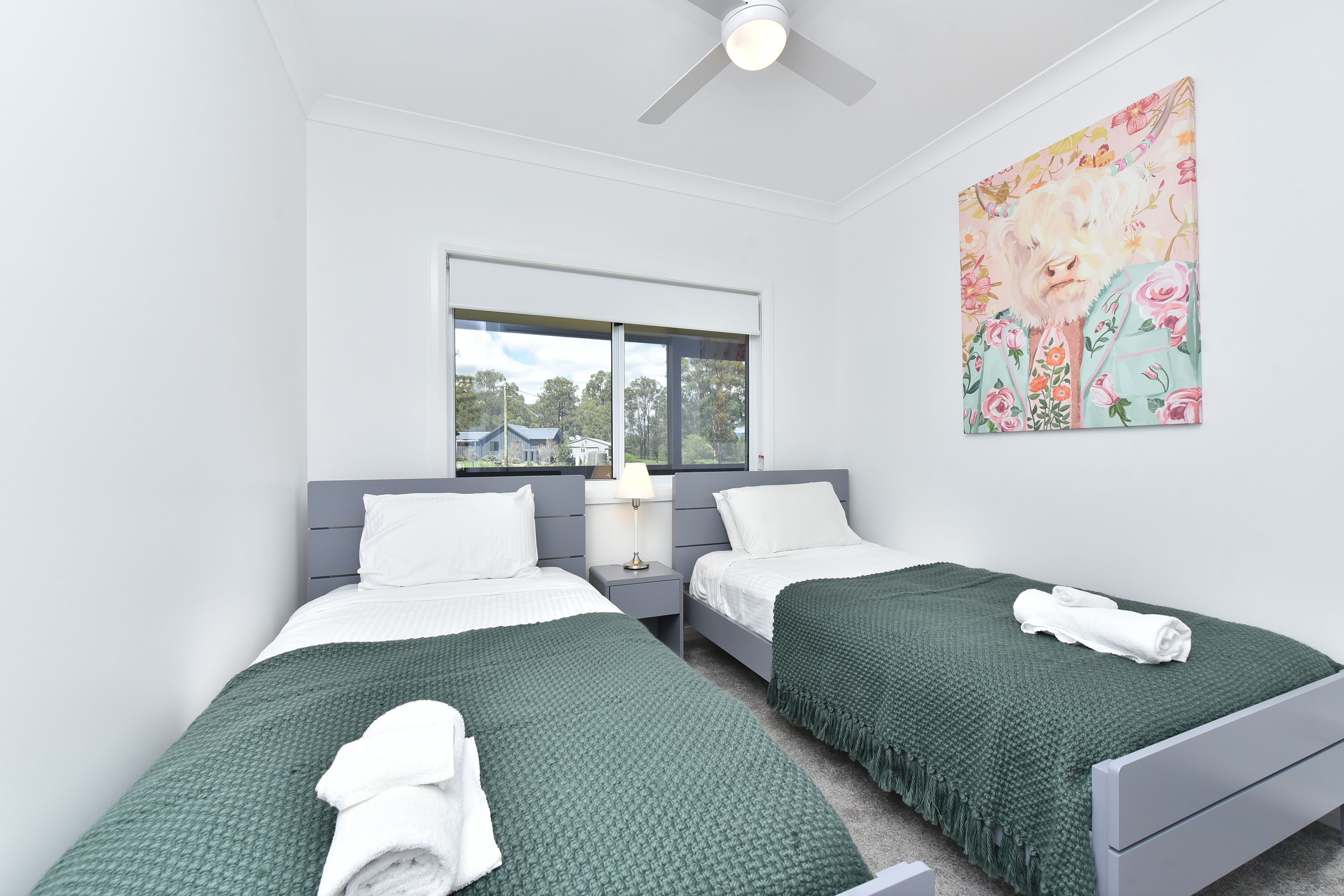 A twin room with two beds, a window, a ceiling fan, and a floral artwork on the wall.