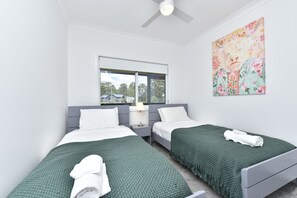 A twin room with two beds, a window, a ceiling fan, and a floral artwork on the wall. - Magpie 2 3 Two for Joy Estate. 3 bedroom (North Rothbury)