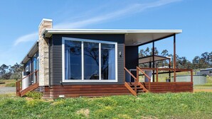 A modern house with a large window, wooden deck, and a clear sky. - Magpie 2 3 Two for Joy Estate. 3 bedroom (North Rothbury)