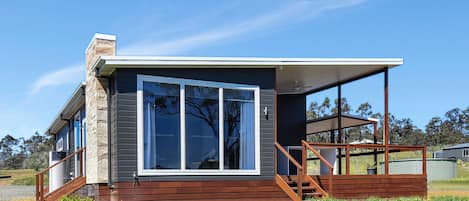 Una casa moderna con un ventanal grande, terraza de madera y cielo despejado.