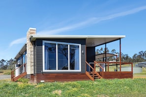 A modern house with a large window, wooden deck, and a clear sky.