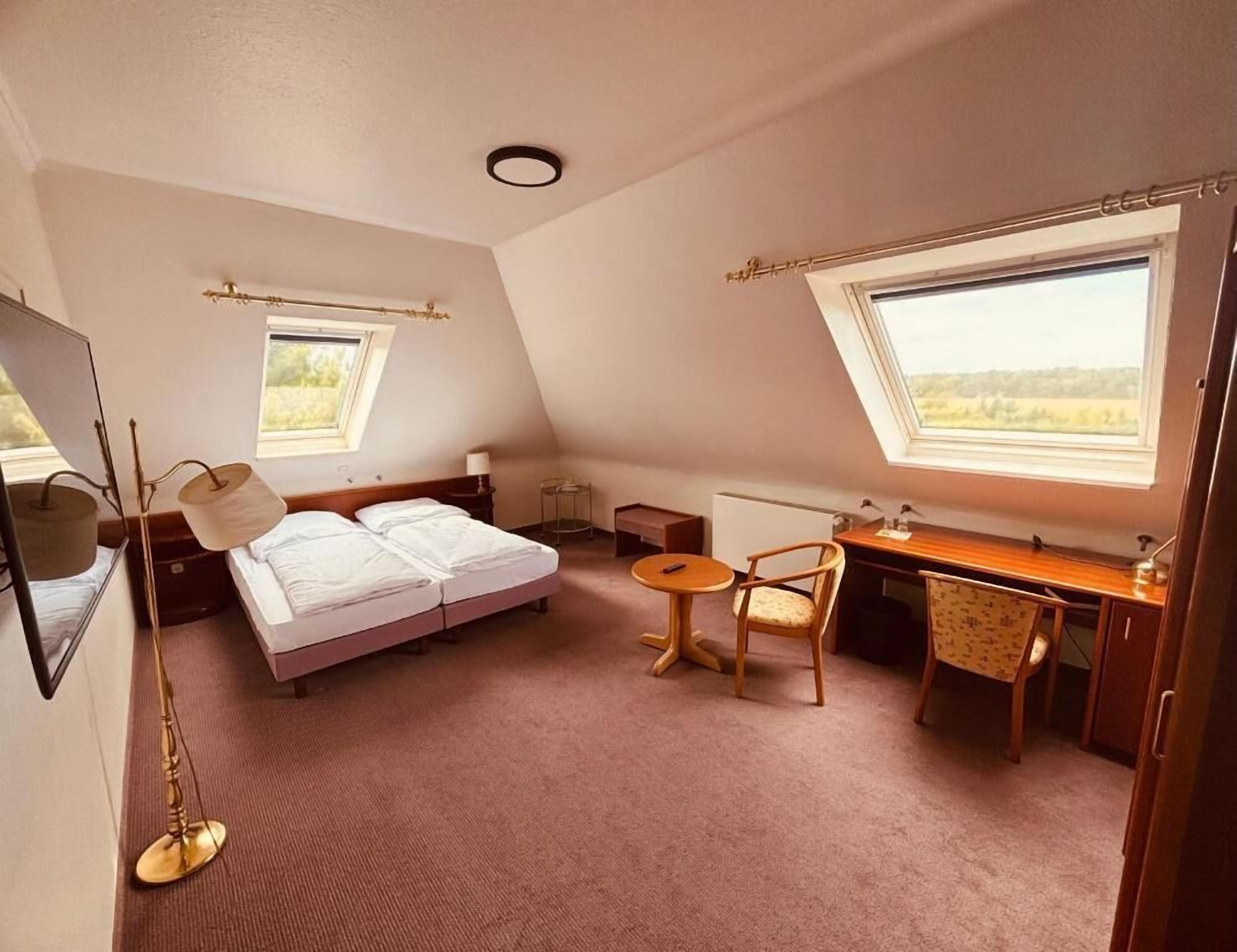 A bedroom with a bed, a desk, a chair, and two windows.