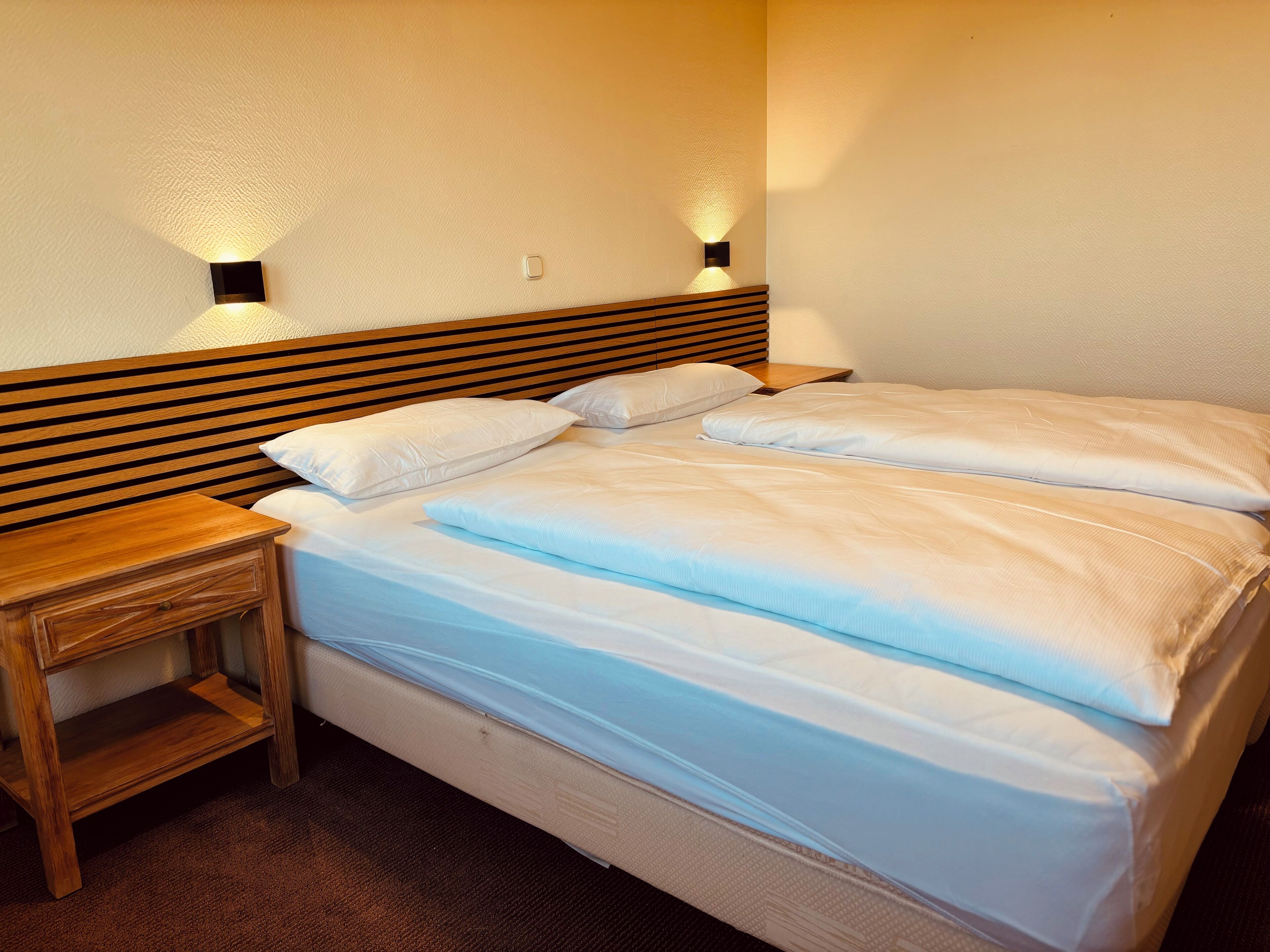 A neatly made bed with white linens and two wall-mounted nightstands.