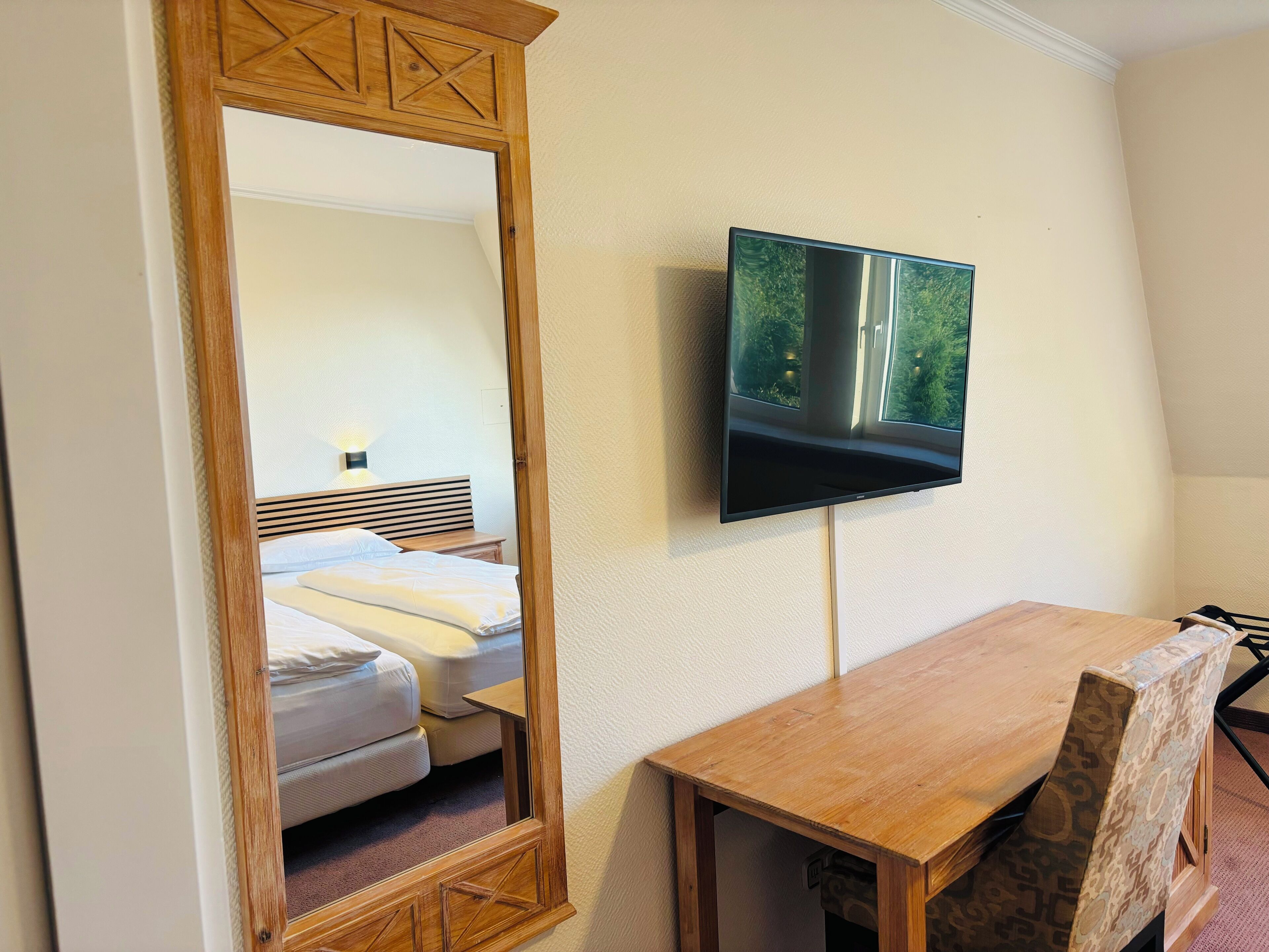 A hotel room with a bed, a TV mounted on the wall, a wooden table, and a chair.