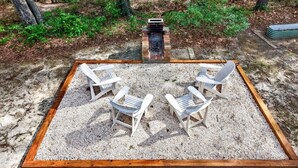 Et firkantet udendørs opholdsområde med fire Adirondack-stole og et bålsted.