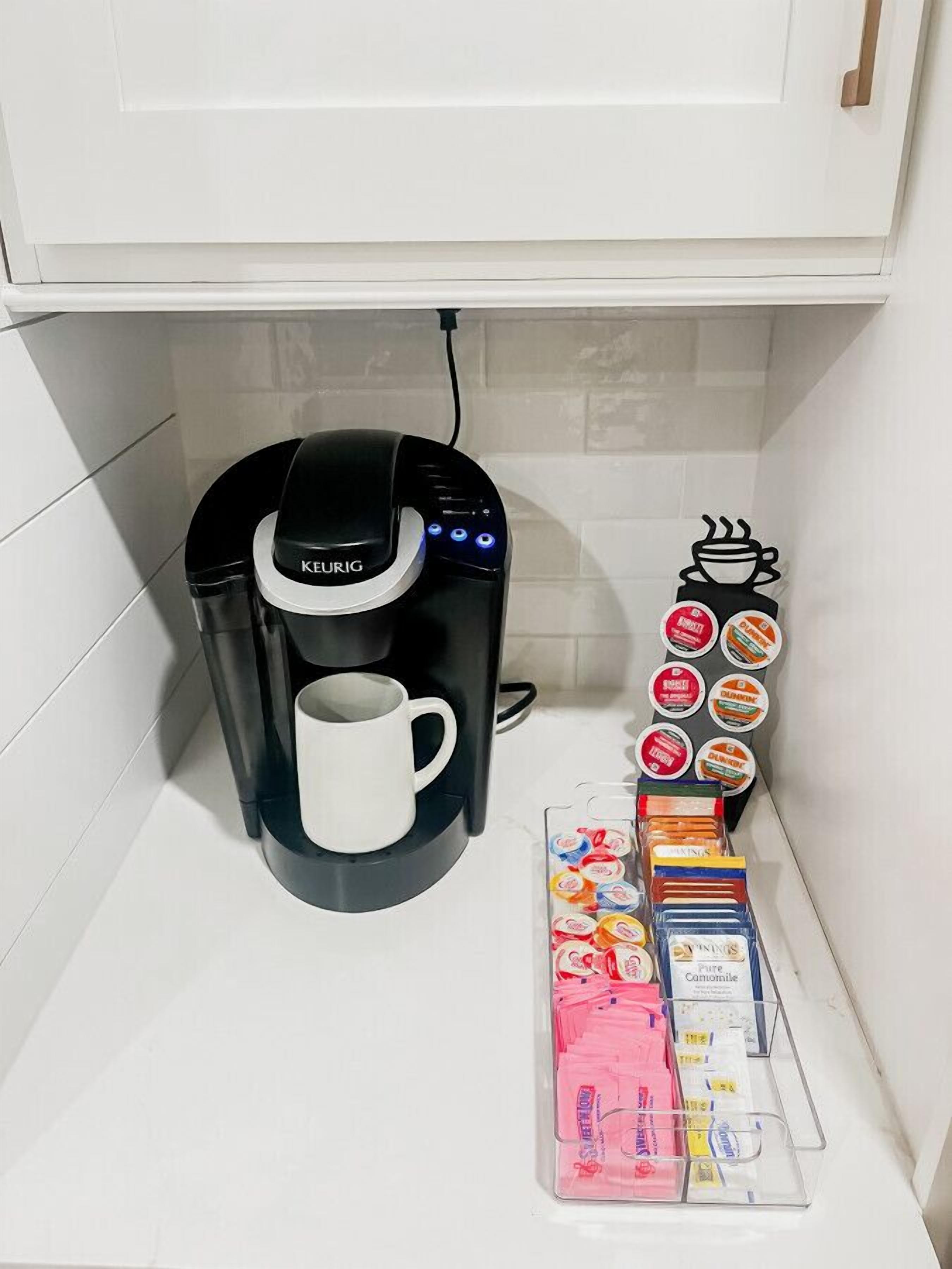 A Keurig coffee maker with a white mug, a coffee pod holder, and a coffee pod dispenser.