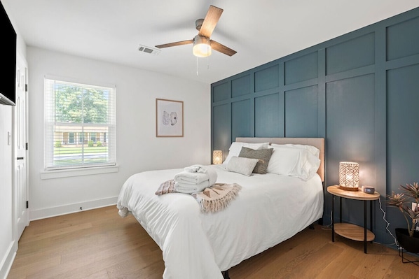 A bedroom with a bed, a ceiling fan, a bedside table with a lamp, and a window with blinds.