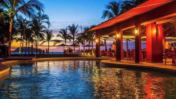 Un espace aménagé au bord de la piscine, offrant une vue sur le coucher de soleil, avec des palmiers et un coin salon abrité.