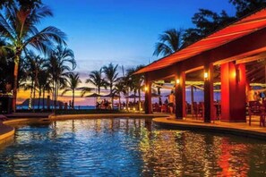 Ein Poolbereich mit Sonnenuntergangsblick, Palmen und einer überdachten Sitzgelegenheit.