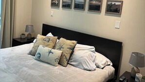 Une chambre à coucher bien rangée, avec un grand lit, une tête de lit et quatre tableaux encadrés accrochés au mur.