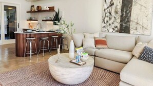 Un salon moderne avec une table basse ronde, un canapé et un coin cuisine équipé de tabourets.