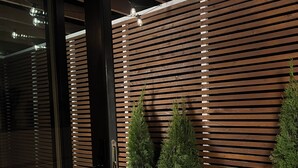 Un intérieur moderne avec des lambris en bois, des jardinières blanches ornées de plantes vertes et une entrée avec une porte en verre.