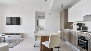 Una cocina moderna con electrodomésticos integrados, un comedor con una mesa grande y sillas, y un televisor de pantalla plana montado en la pared.
