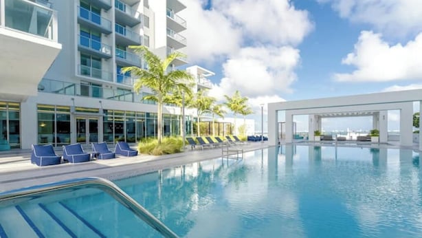 A modern hotel with a large indoor swimming pool, lounge chairs, and palm trees. - Experience Design District, Pool, Gym and Parking (Miami)