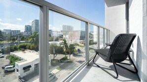A balcony with a view of a cityscape, a black wicker chair, and a white building in the background. - Experience Design District, Pool, Gym and Parking (Miami)