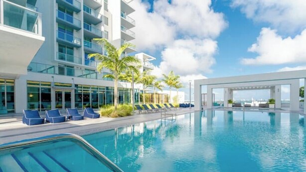 A modern hotel with a large indoor pool, lounge chairs, and palm trees. - Modern Design District Condo, Balcony, Pool, Gym (Miami)
