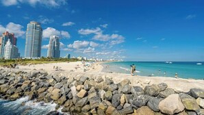 A beach with rocky shoreline, clear blue sky, and tall buildings in the background. - Modern Design District Condo, Balcony, Pool, Gym (Miami)