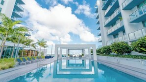 A modern hotel with a swimming pool, palm trees, and a clear blue sky. - Relax with Pool, Gym, Balcony in Design District (Miami)