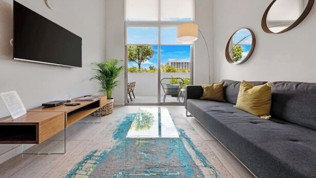 A modern living room with a sofa, a coffee table, a TV, and a view of the outdoors. - Relax with Pool, Gym, Balcony in Design District (Miami)