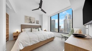 Ein modernes Schlafzimmer mit einem großen Bett, einem Schreibtisch und Blick auf hohe Gebäude.