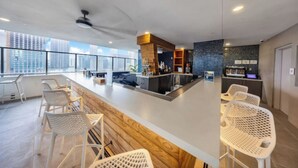A modern bar area with a wooden accent wall, white bar stools, and a city view through large windows. - Penthouse Studio in heart of Miami w pool & gym (Miami)