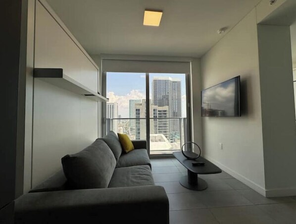 A modern living room with a grey sofa, a small table, and a TV mounted on the wall.
