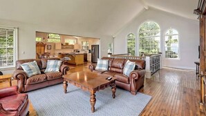 Un salón amplio con sofás de cuero, una mesa de centro de madera y vistas a la cocina y el comedor a través de grandes ventanales.