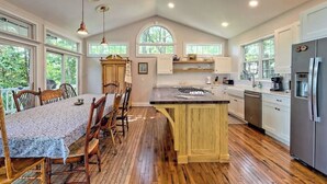 Una cocina amplia con una isla grande, suelo de madera y abundante luz natural gracias a sus ventanas grandes.