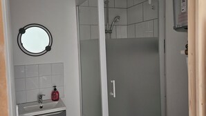 Et badeværelse med et brusebadeværelse med glasvægge, en vask med spejl og et lille skab.