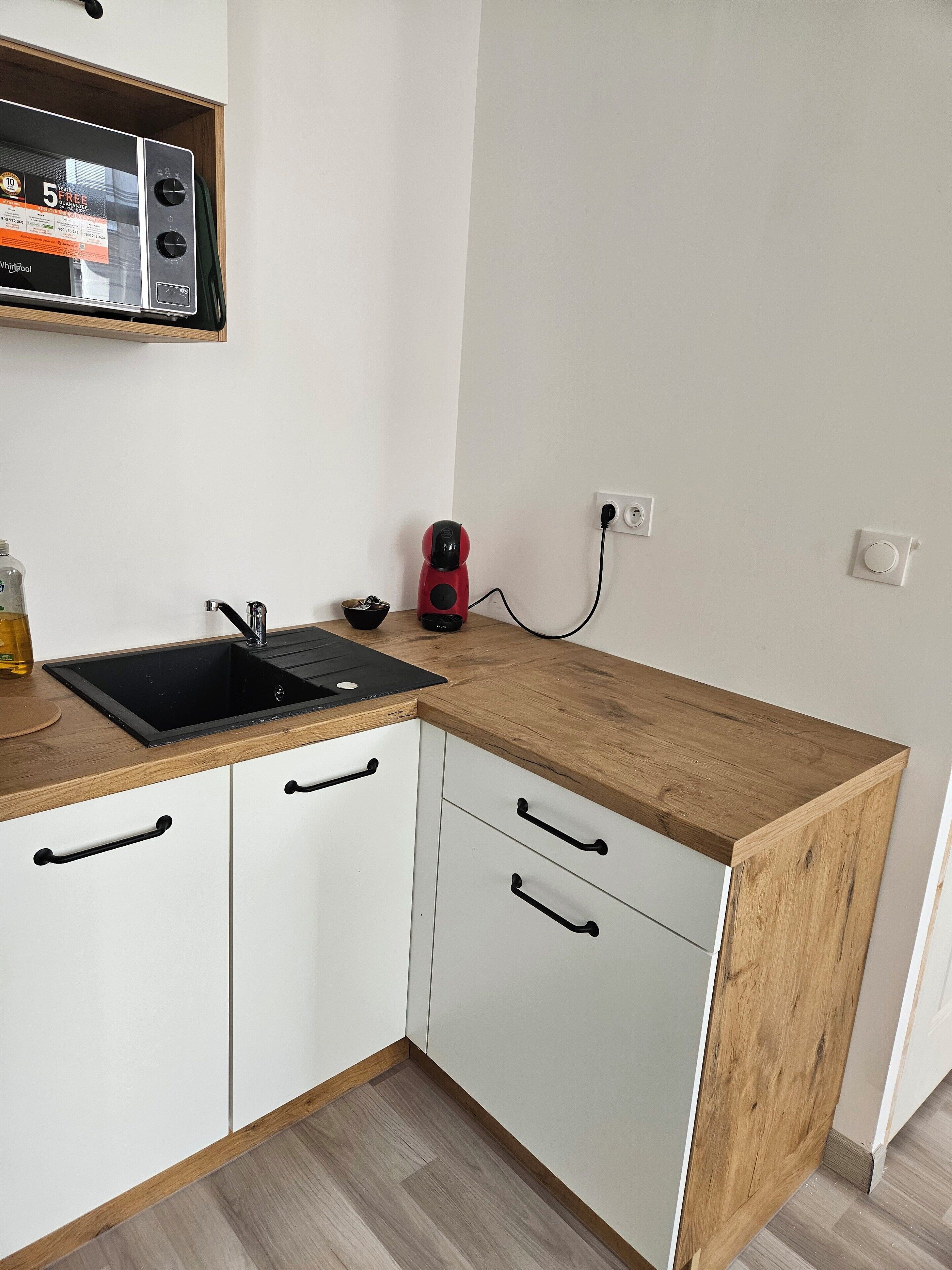 Una cocina compacta con encimera de madera, un lavabo negro y armarios blancos.