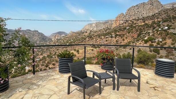 An outdoor seating area with two chairs and a table, surrounded by potted plants and overlooking a mountainous landscape. - Awesome home in El Chorro, Alora (El Chorro, Alora)
