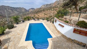 A rectangular swimming pool with a stone patio, surrounded by a white wall with terracotta tiles, set against a mountainous backdrop. - Awesome home in El Chorro, Alora (El Chorro, Alora)