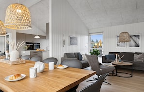 Un salon moderne avec une table à manger en bois, des canapés gris et une cuisine en arrière-plan.
