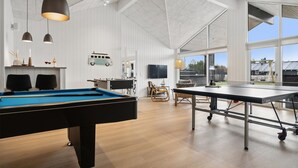 Una habitación amplia con mesa de billar, mesa de ping pong y un gran ventanal con vistas al exterior.