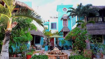 Un patio tropical con edificios de techo de paja, una fuente central y abundante vegetación.