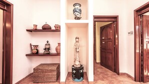 A hallway with a statue on a pedestal, shelves with pottery, and a wooden door.
