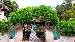 A gated entrance with a stone wall, potted plants, and a thatched roof structure.