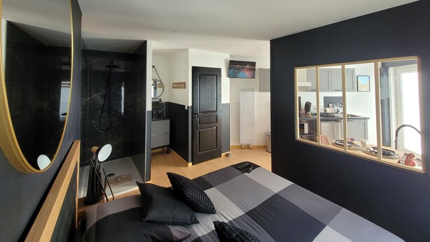 A modern bedroom with a large bed, a mirror, a TV, and a view into the kitchen. - The black tendance, maxi studio hyper center, 1km from train station, tourism/business (Calais)