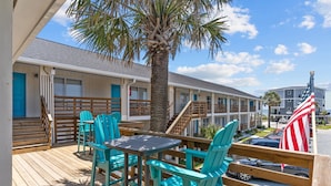 A motel with a wooden deck, turquoise chairs, and a palm tree.